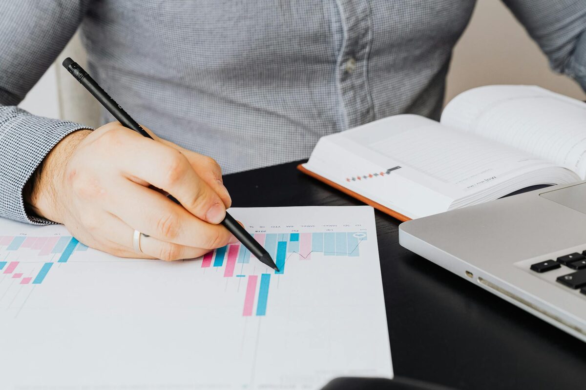 Person writing on paper with graphs next to a laptop — solo creator content analytics weekly tracking template