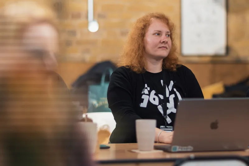 A woman at a laptop in a focused work session, writing and reviewing content with notes nearby