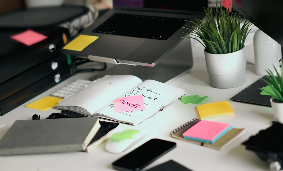 A solo creator at a cluttered desk with a laptop, notebooks, and checklists mapping out a content repurposing plan