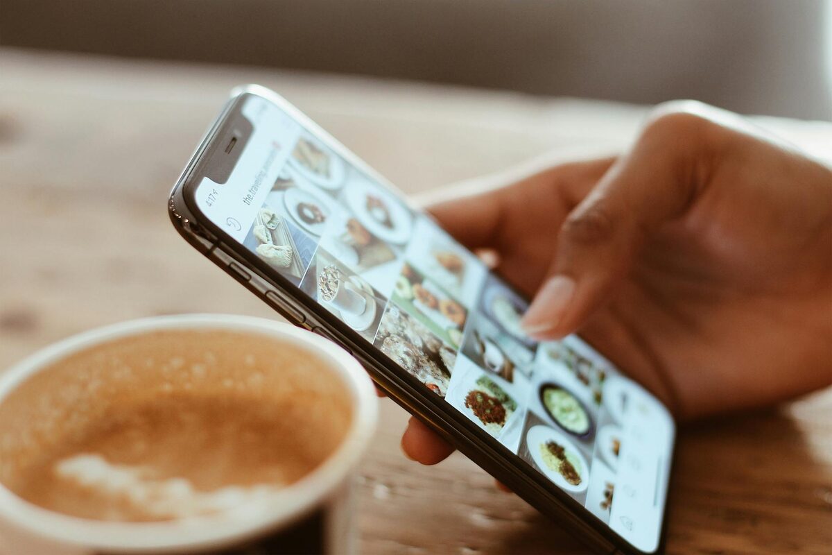 Hand browsing social media photos on a smartphone beside a coffee cup, showing what to post on Instagram for lead capture