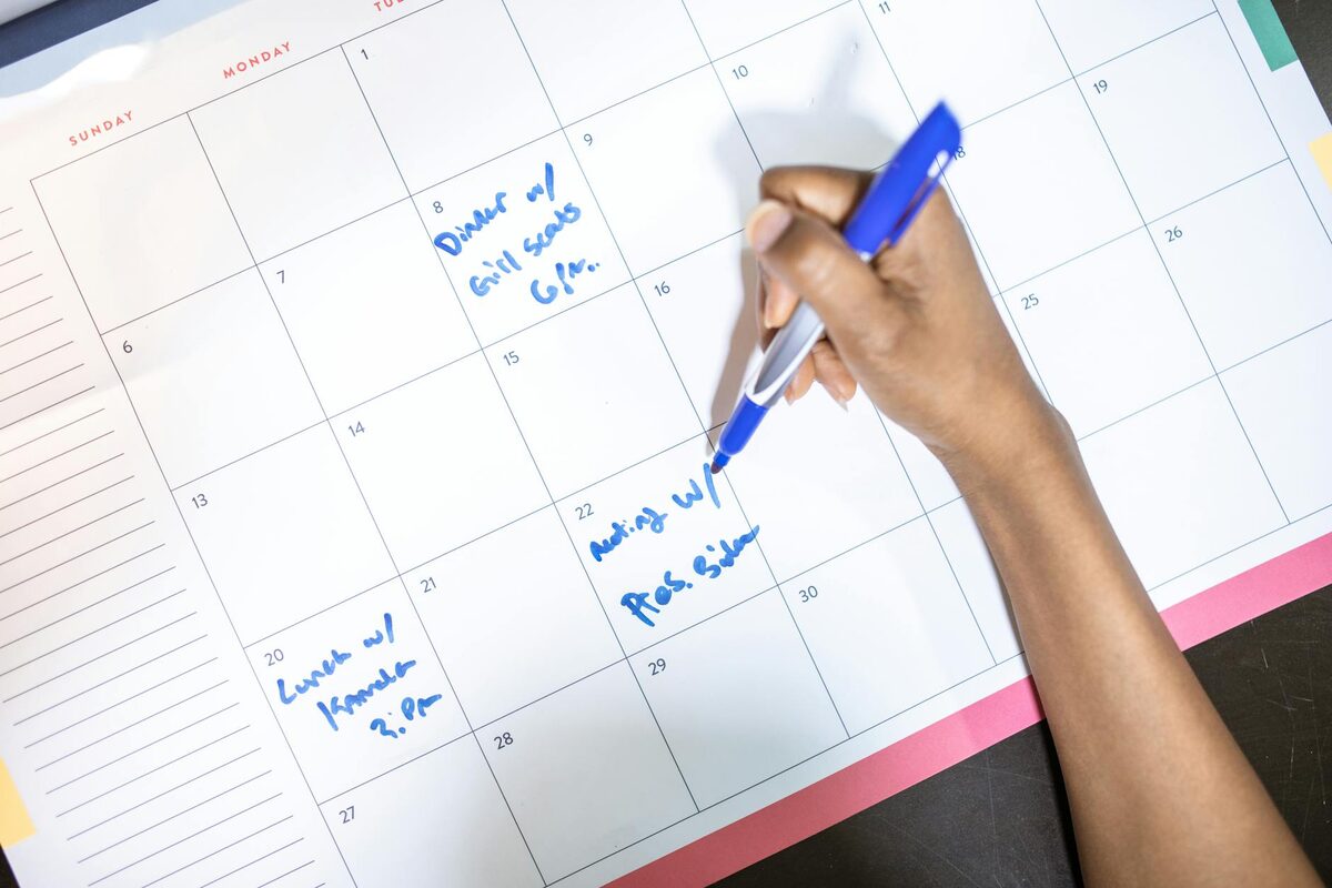 Person writing appointments on a calendar, representing a content scheduling queue for solo creators